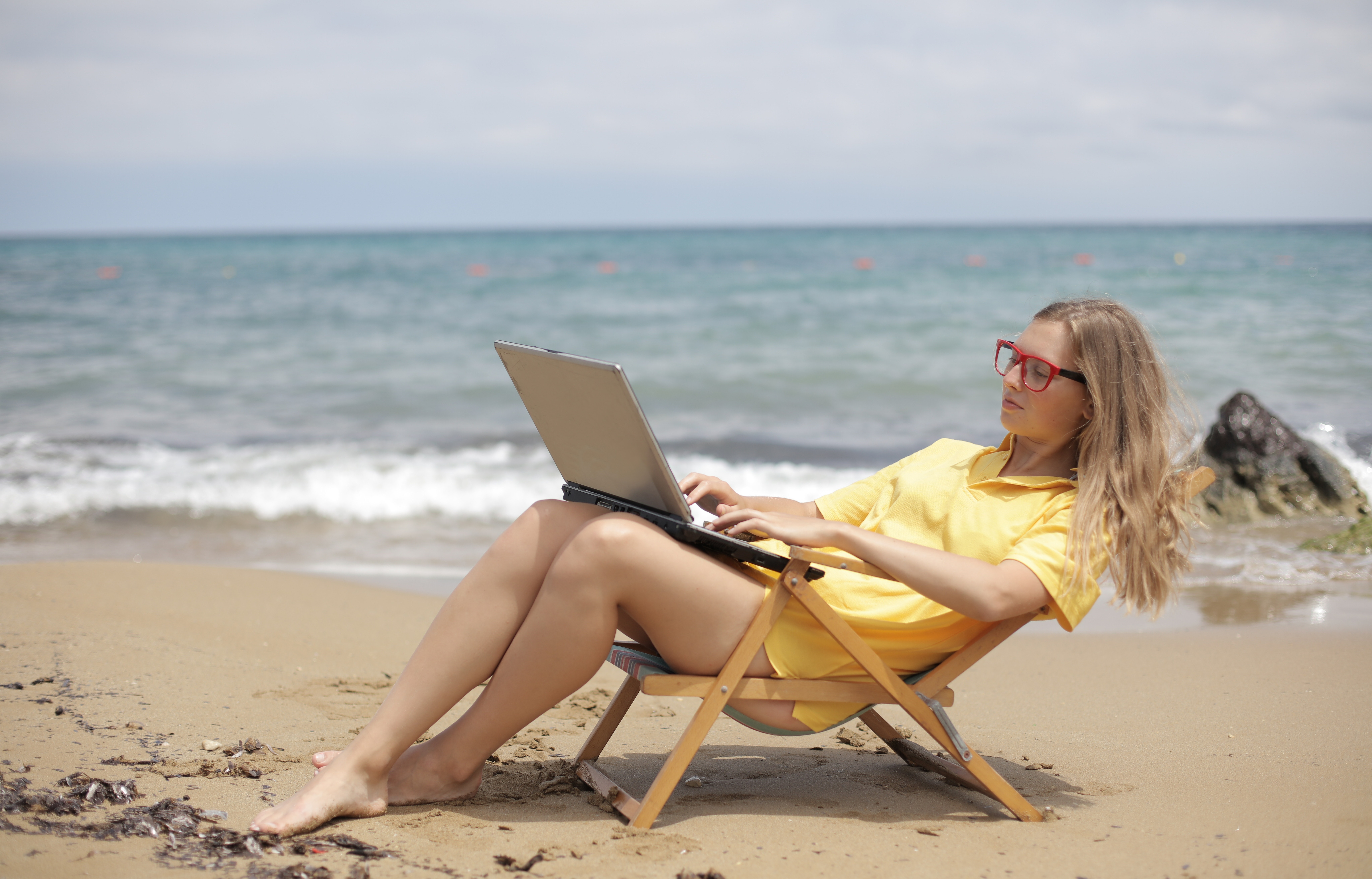 Woman in yellow tshirt on the beach in a lounge chair working on her computer.