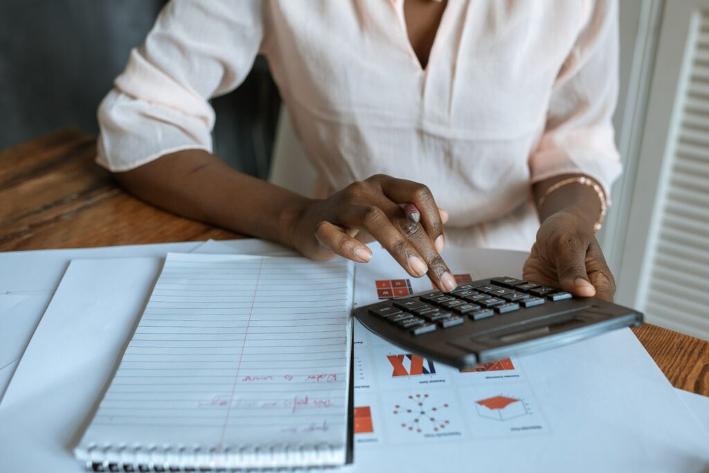 Dark skinned woman at a desk working with a calculator and papers.