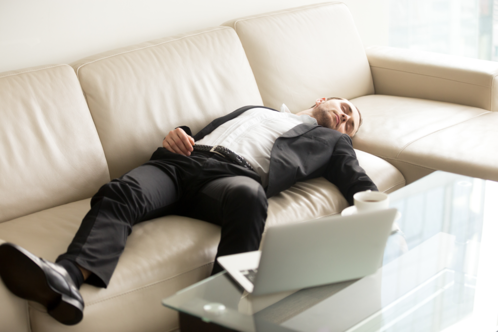 Man in suit laying on couch with laptop on coffee table nearby