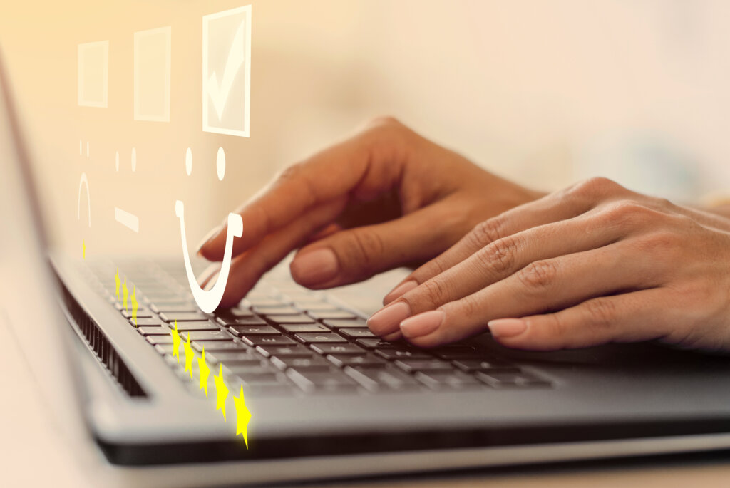 an image showing a smiley emoji and a hand typing on a laptop