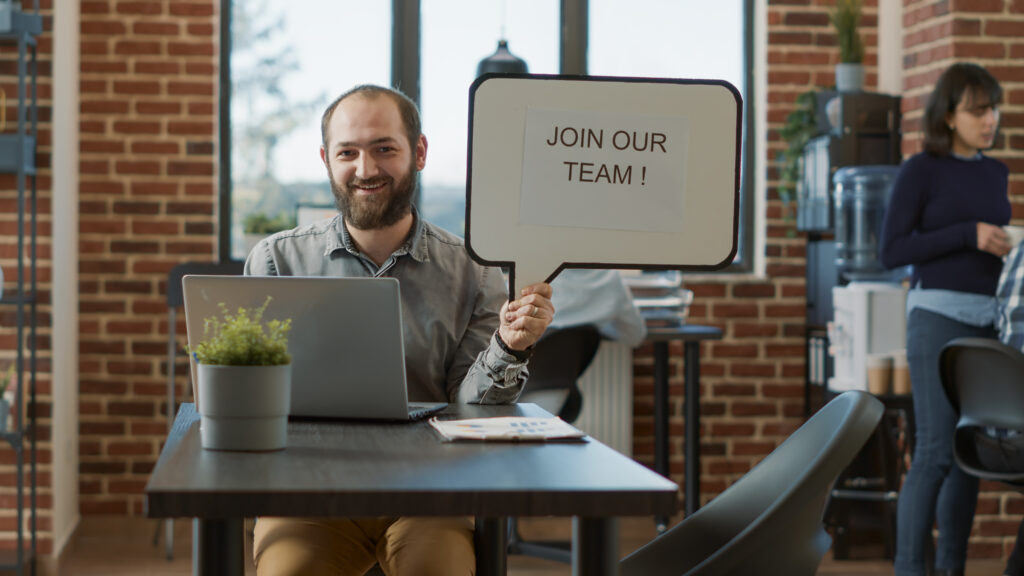 Man trying to post a job while holing a sign that says 'join our team'