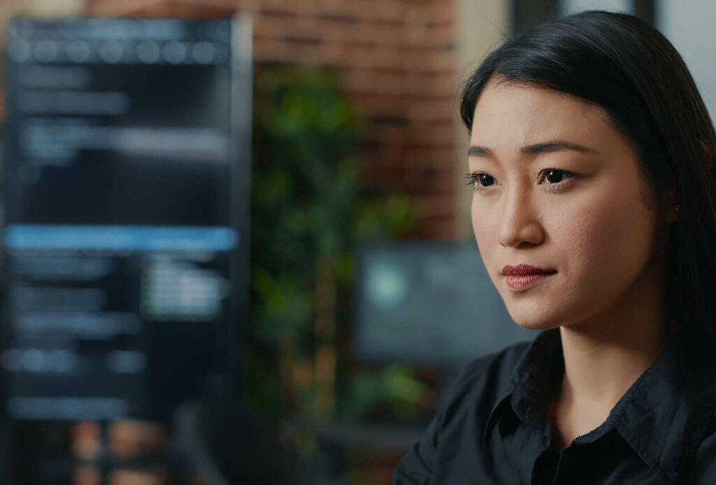 Focused asian software developer writing programming code and smiling sitting at desk in database development agency. Friendly coder computing big data casually in it startup office.