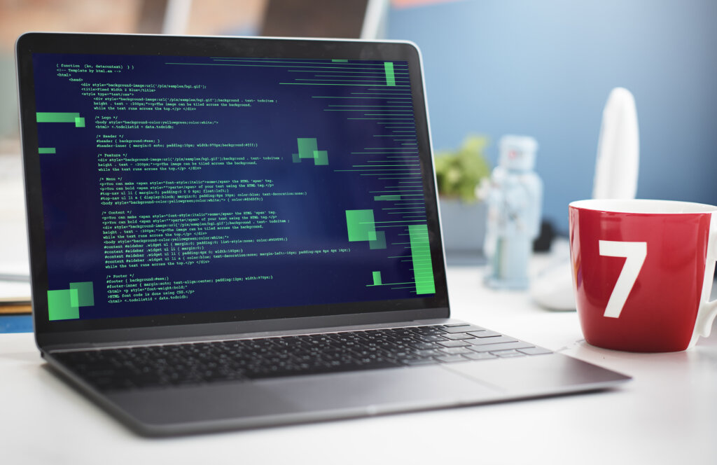Computer with lots of code on the screen next to a cup of coffee