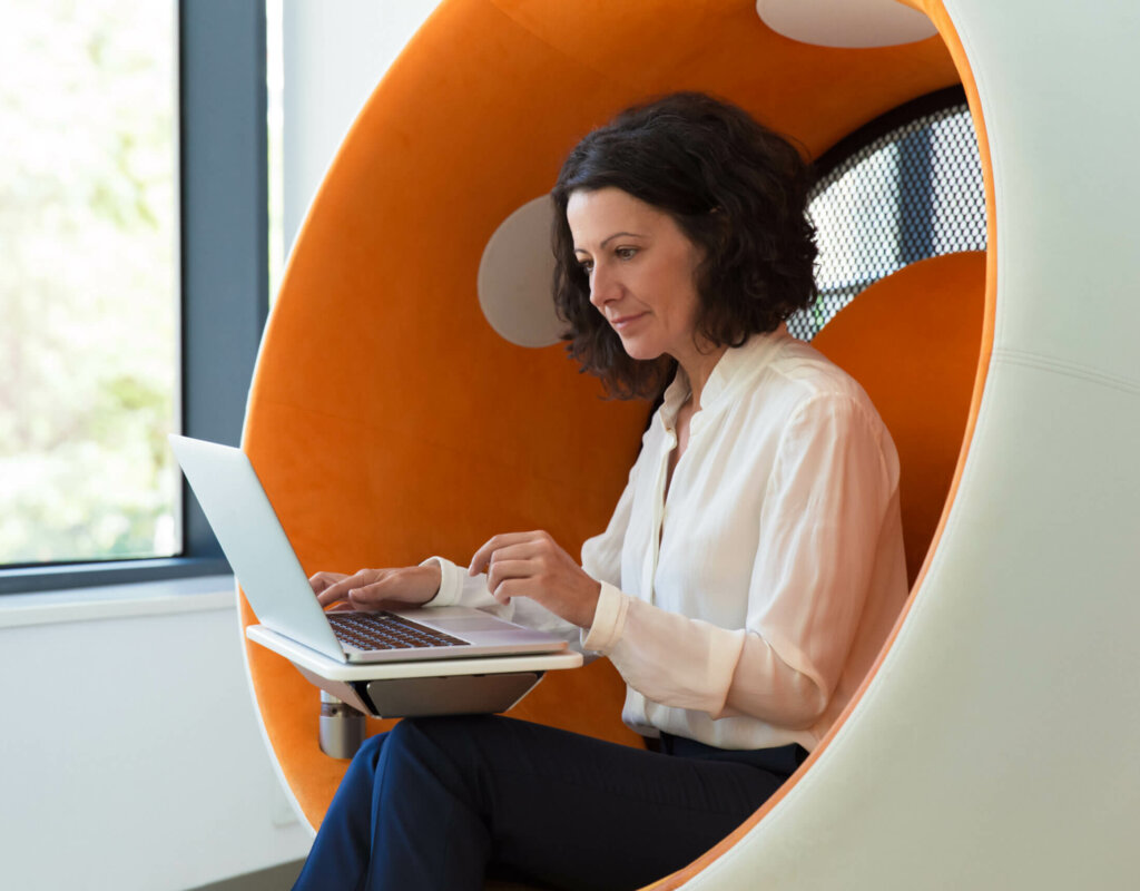 Serious confident businesswoman working on computer in office lounge. Business woman sitting in interactive chair, using laptop, staring at screen. Office rest room concept