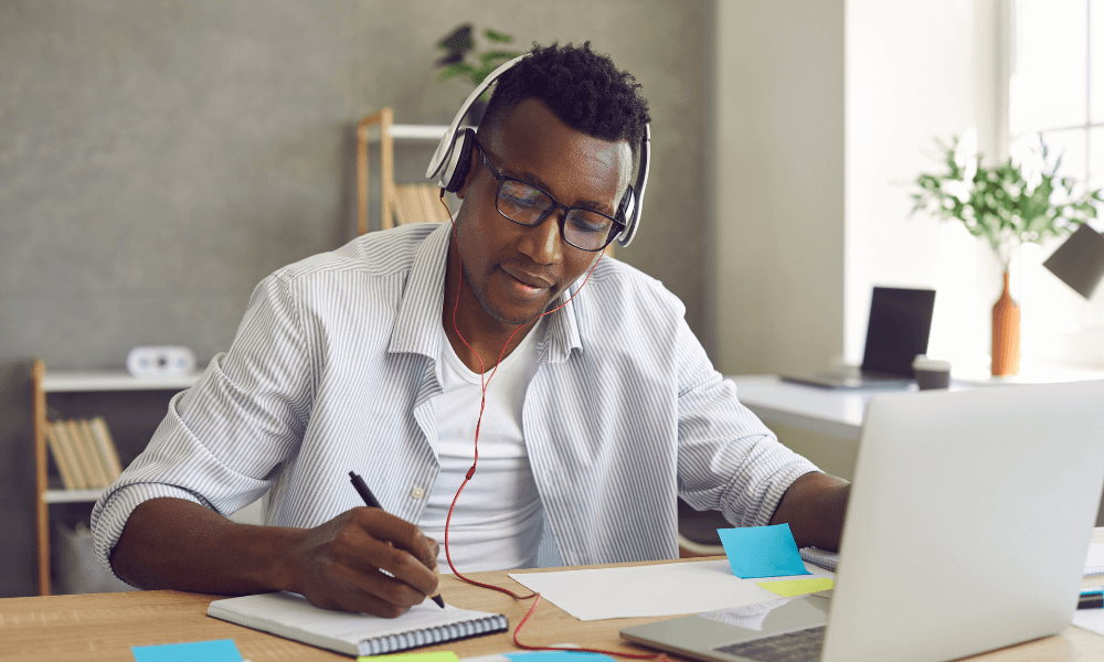 Black Virtual Assistant with headphones on taking notes in front of a laptop