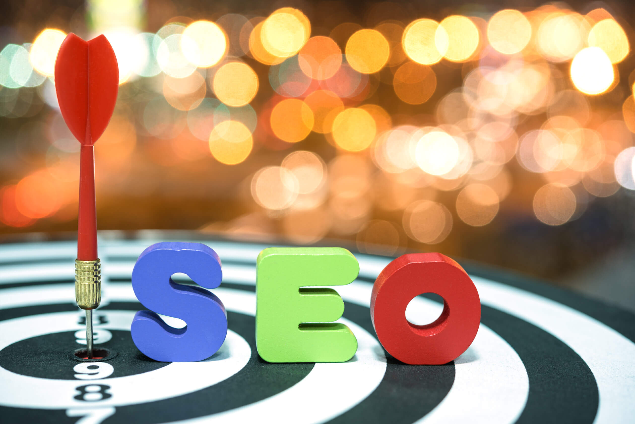 Search Engine Optimization target marketing concept with red dart target hitting in bullseye on dartboard and colorful alphabet wood letters SEO over light blurred bokeh background