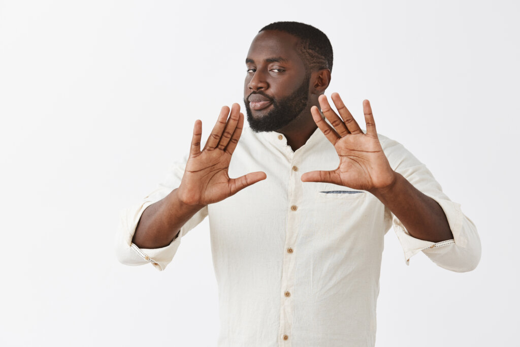 Easy man I got it. Serious-looking calm and confident professional African American businessman in white shirt raising palms near chest and gazing with self-assured expression at camera, calming down. Copy space