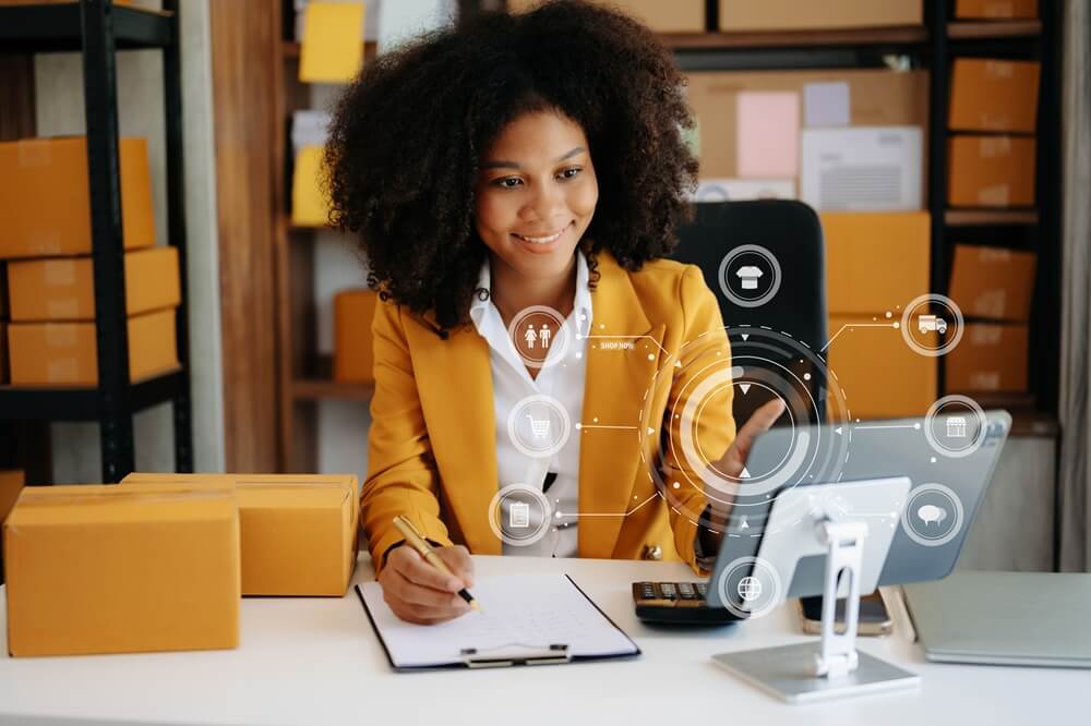 African Woman hand using a laptop, smartphone and tablet and writing notebook at the office of her business online shopping. In home with virtual icon