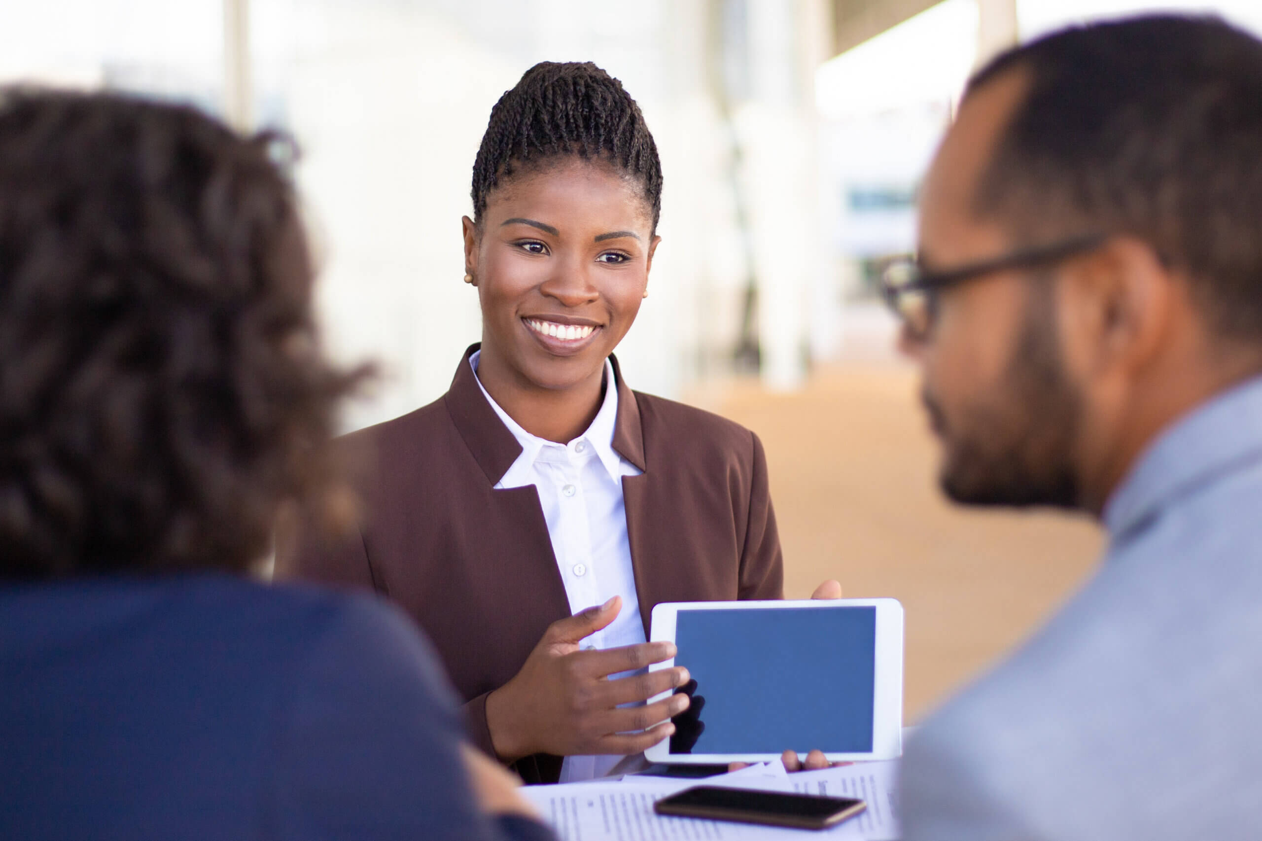 Joyful successful sales agent presenting content on tablet to clients. African American business woman speaking, smiling and showing blank tablet screen to colleagues or partners. Negotiation concept